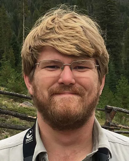 Tom Johnson smiling with glasses and beard outdoors.